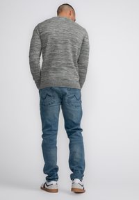 Gray textured sweater with a round neckline, paired with light blue jeans. Footwear includes white and gray sneakers with black accents.