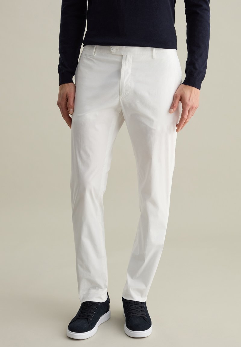 Pantalons en coton blanc à coupe slim, avec fermeture éclair et poches latérales, associés à des baskets en suède bleu marine avec des semelles blanches.