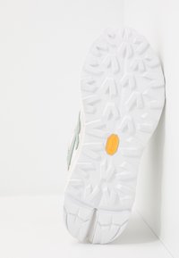 Vibram sole with textured white rubber, featuring aggressive treads. Upper has a woven light green and beige design with minimal accents.