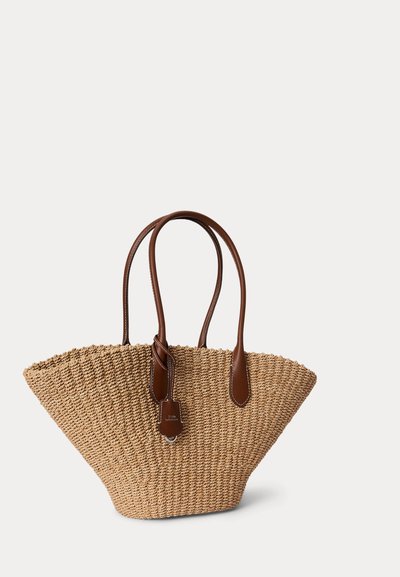 Szövött szalmatáska széles, szögletes formával és barna bőrfogalmakhoz, egy fogantyúhoz csatlakoztatott kis bőrcímkével.