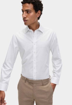 Witte langemouwen dress shirt met een puntige kraag en knopen aan de voorkant, gecombineerd met lichtbruine broeken. Gladde stof zonder patronen.