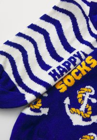 Calze a righe orizzontali blu e bianche con motivi di ancore. Il testo "HAPPY SOCKS" appare in giallo sulla zona della caviglia.