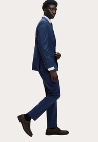 Niebieski garnitur o dopasowanym kroju, z jednoprzodowym żakietem i pasującymi spodniami. Brązowe buty typu double monk strap. Biała koszula pod spodem.