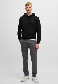 Svart hoodie med framficka och dragsko på huven, i kombination med grå byxor och beige sneakers. Snyggt tyg, enkel design, utan mönster.