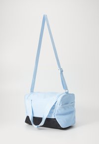 Bolsa de tela azul claro con fondo negro, asas cortas y una correa larga ajustable. Textura suave con cierre de cremallera y bolsillo lateral.