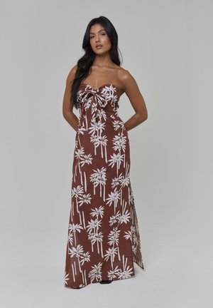 Robe longue marron sans bretelles avec motif de palmiers blancs. Elle comporte un nœud à l'avant et un tissu fluide et texturé.