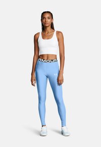Svetlo modre oprijete leggins hlače z črnim pasom, na katerem je napis "ARMOUR", v kombinaciji z belo skrajšano majico brez rokavov. Gladka tekstura.