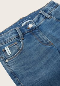 Modré džíny z denimu s předními kapsami, poutky na pásek, kovovým knoflíkem a bílou štítkem s nápisem "Tom Tailor" na malé přední kapse.