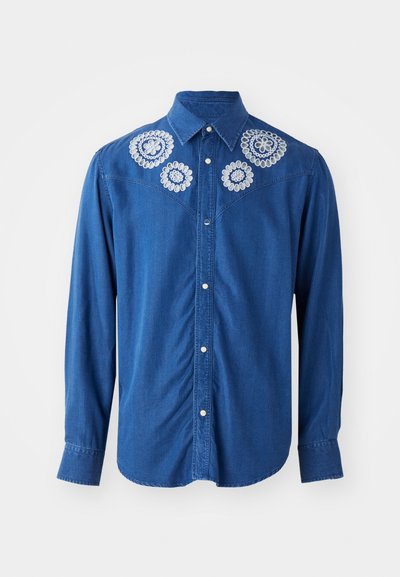 Blaues Jeanshemd mit langen Ärmeln, das weiße Blumenstickerei auf der Brust und den Schultern aufweist. Klassischer Kragen und durchgehende Knopfleiste.