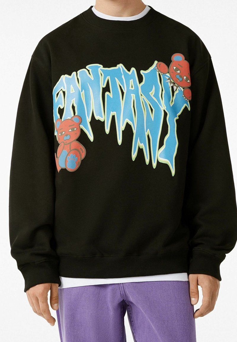 Svart sweatshirt med djärv "FANTASY" grafik i blått och grönt, med tecknade björnakcenter. Ribbad mudd och fåll, avslappnad passform.