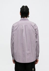 Férfi gombos ing függőleges lila és fehér csíkokkal, hosszú ujakkal és klasszikus gallérral. Az anyag könnyűnek tűnik, laza szabású.