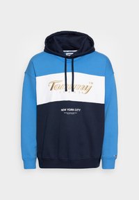 Felpa con cappuccio blu, bianca e blu navy; presenta il logo dorato "Tommy Jeans" e il testo "NEW YORK CITY" sul davanti; tessuto in misto cotone.
