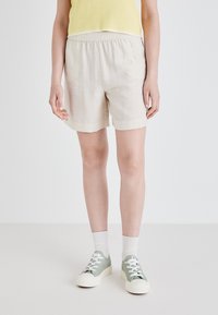 Lyse beige linshorts med elastisk midjebånd, med en avslappet passform og sidelommer, sammen med grønne snøresko.