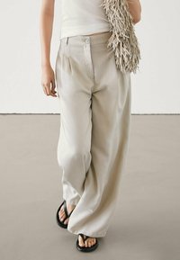 Light beige wide-leg trousers made of a smooth fabric, featuring a front button closure and side pockets. Paired with black flip-flops.