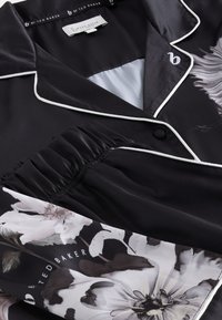 Fekete selyem pizsama felső fehér csíkozással, szürke és krémszínű virágmintás díszítéssel, valamint begyűrt ujjkialakítással.