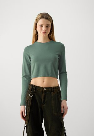 Green cropped long-sleeve shirt made of soft material, paired with dark cargo pants featuring pockets and metal hardware accents.