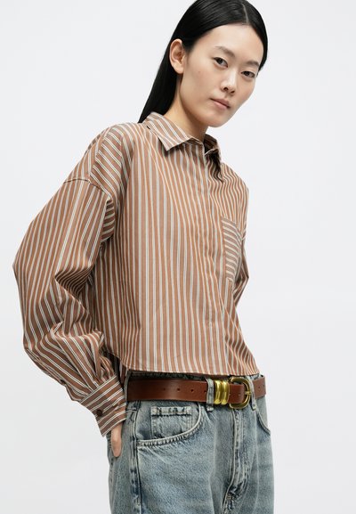 Pruunide ja valgete triipudega triiksärk kraega, laiade varrukate ja esitaskuga; kantud kõrge vöökohaga helesiniste teksade ja pruuni vööga.