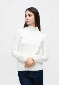 Λευκό πουλόβερ με μακριά μανίκια και ψηλό λαιμό, από λεία, ελαστική ύλη. Εφαρμοστή γραμμή με ριμπ λαιμό και μανσέτες. Συνδυάζεται με σκουρόχρωμο τζιν.