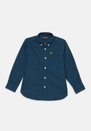 Chemise bleu foncé à manches longues avec boutons, poche avant et petit logo jaune brodé sur la poche, étalée à plat sur fond blanc.