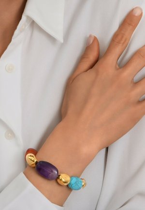 Le bracelet en perles présente des pierres d'améthyste, de turquoise et d'agate orange avec des accents dorés. Le design est lisse et arrondi, ce qui renforce l'attrait visuel.