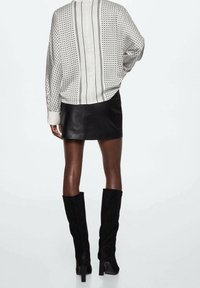 Long-sleeve blouse in white with black polka dots and vertical stripes, paired with a black leather mini skirt and knee-high suede boots.