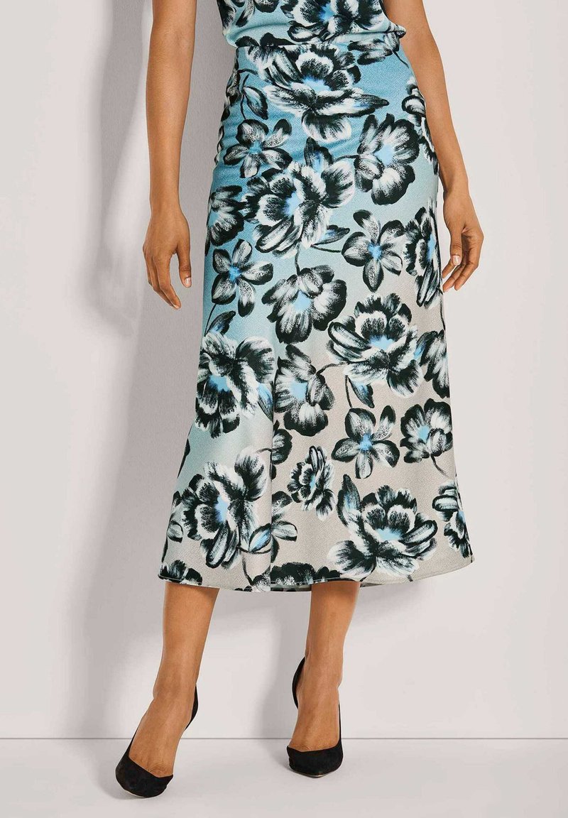 Florale Midirock mit blauen, schwarzen und weißen Blumenmustern auf hellem Hintergrund. Glattes Material, ausgestellte Form, getragen mit schwarzen High Heels.
