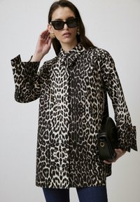Oversized shirt met luipaardprint, met een kraag, lange mouwen en zijsplitten, gecombineerd met een zwarte handtas. Haar los en een zonnebril op.