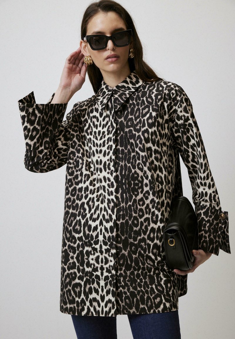 Oversized shirt met luipaardprint, met een kraag, lange mouwen en zijsplitten, gecombineerd met een zwarte handtas. Haar los en een zonnebril op.