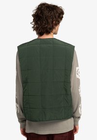 Groene gewatteerde vest gemaakt van lichtgewicht materiaal, met een ruitpatroon en een ronde halslijn, gedragen over een grijs shirt met lange mouwen.