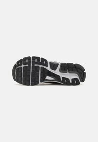 Semelle de chaussure de sport en noir et blanc avec un caoutchouc texturé, présentant un motif en grille et un profil prononcé pour une bonne adhérence et durabilité.