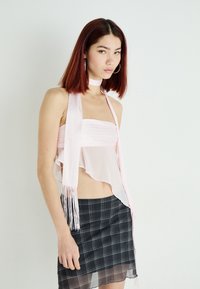 Top di raso rosa con un design fluido e a strati, bordi frangiati, abbinato a una mini gonna a quadri nera con orlo trasparente.