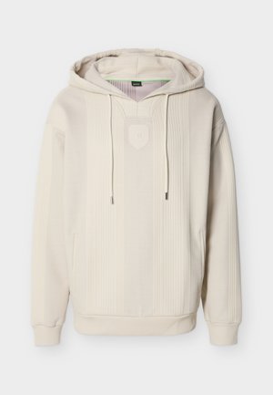 Beige huppari, jossa on teksturoitu kuvio, etutasku, kiristysnyörit ja kilven muotoinen logo rinnassa. Pehmeä kangaspinta.