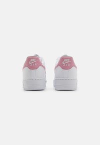 Biele tenisky Nike Air s ružovými akcentmi na päte. Hladký kožený materiál, plochá podrážka a biele švy. Logo je výrazne zobrazené.