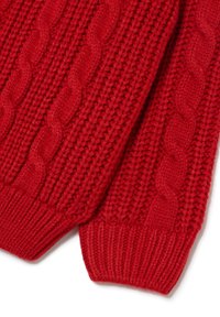 Dichtbijzicht van een rode gebreide stof met kabel- en ribbelpatronen, met de nadruk op de textuur en steekdetails op de mouwen van het kledingstuk.