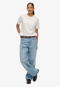 Biała bawełniana koszulka z krótkim rękawem, noszona z jasnoniebieskimi szerokimi spodniami jeansowymi, brązowym plecionym paskiem oraz czarnymi butami z teksturowaną podeszwą.