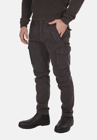 Pantaloni cargo grigio scuro con numerose tasche, design affusolato e tessuto testurizzato. Presentano cuciture resistenti e stivali neri coordinati.