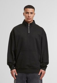 Black pullover sweatshirt featuring a high collar with a front zipper, long sleeves, and a kangaroo pocket. Made from soft, textured fabric.