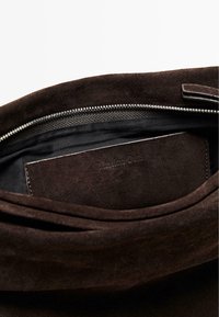 Intérieur d'un sac en daim marron avec une texture douce, comportant une fermeture zippée et une étiquette en cuir embossée avec "Massimo Dutti."