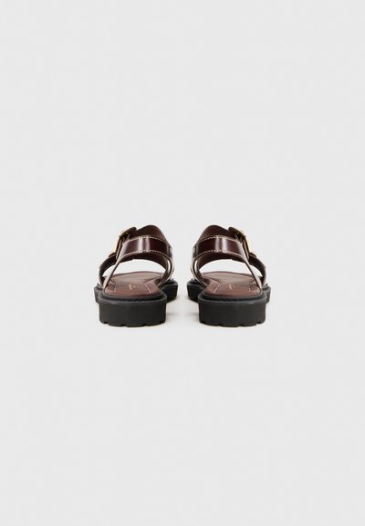 Mørkebrune sandaler med en blank overflade, justerbare remme og en polstret sål. Sort gummiydersål med tekstureret slidbane for godt greb.