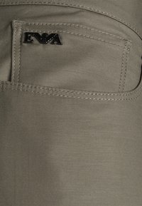 Šedá tkanina s zadní kapsou s prošíváním a kovovou destičkou s logem s vyraženým nápisem "EVA". Hladký povrch, jednoduchý design.