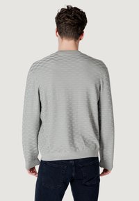 Lichtgrijze trui met een gestructureerd ruitpatroon, geribde manchetten en zoom, gedragen met donkerblauwe spijkerbroek.