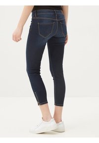 Jeans ajustados de color azul oscuro con cintura alta, con dobladillos en los tobillos con cremallera y dos bolsillos traseros. Fabricados en denim con una textura suave.