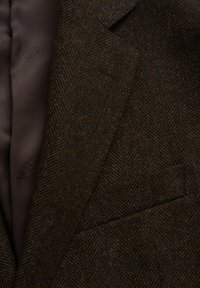 Blazer marrone con motivo a spina di pesce, realizzato in lana testurizzata, con fodera in satin marrone e taschino. Branding discreto visibile.
