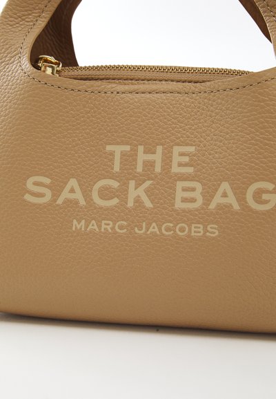 Kahva ruskea laukku rakenteellisella muodolla, jossa on kohokuvioitu teksti "THE SACK BAG" ja "MARC JACOBS", kultainen vetoketju ja teksturoitu pinta.