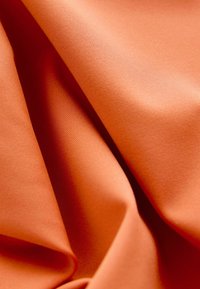 Tekstuuriga kangas soojas oranžis toonis, millel on sujuvad, voolavad voldid, kergelt läikiv pind ja peen, ühtlane kootud muster.