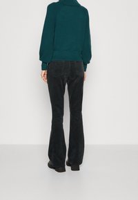 Teal knitted sweater with textured sleeves, high collar, paired with black flared corduroy pants. Smooth fabric, fitted design, and low heel boots.