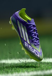 Purple and neon green football boot with a textured, striped design, featuring six studs on a translucent sole and laces along the front.