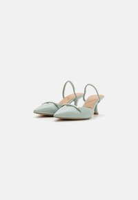 Svetlozeleni lakirani slingback cipele s šiljastim vrhom, s zlatnim naglaskom na prednjem dijelu i zakrivljenim potpeticom srednje visine.