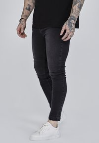 Svart slim-fit jeans i denim med en slät textur och minimala detaljer, kombinerat med vita sneakers.