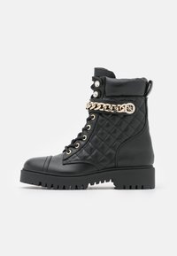 Botas de tobillo de cuero negro acolchado con acento de cadena dorada, parte delantera con cordones, punta redondeada y suela de goma estriada. Presenta botones decorativos.